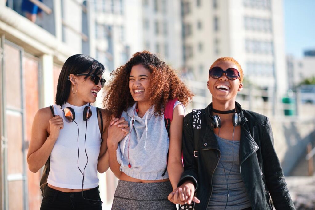 Women friends, holding hands and walk in city with smile, support or happiness for summer travel together. Black woman students, laughing and comic joke with excited face, happy and group vacation.